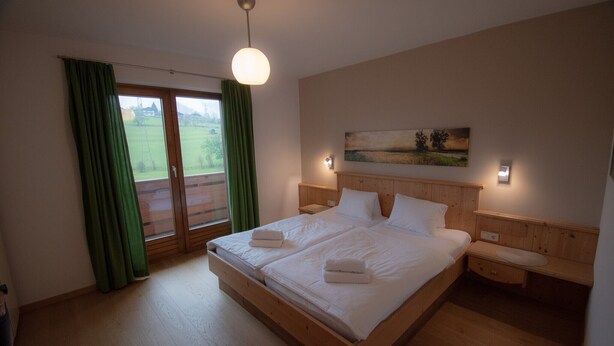 A double bed with a wooden headboard, a nightstand, and a painting on the wall. - Hochkönig 4 Apartment (Embach)