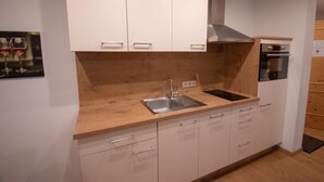A modern kitchen with white cabinets, a wooden countertop, a stainless steel sink, and a built-in oven. - Hochkönig 4 Apartment (Embach)