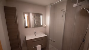 Un baño moderno con ducha envuelta en vidrio, tocador con espejo y mueble de madera.