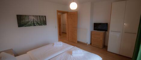 A bedroom with two beds, a wooden wardrobe, a television, and a radiator.