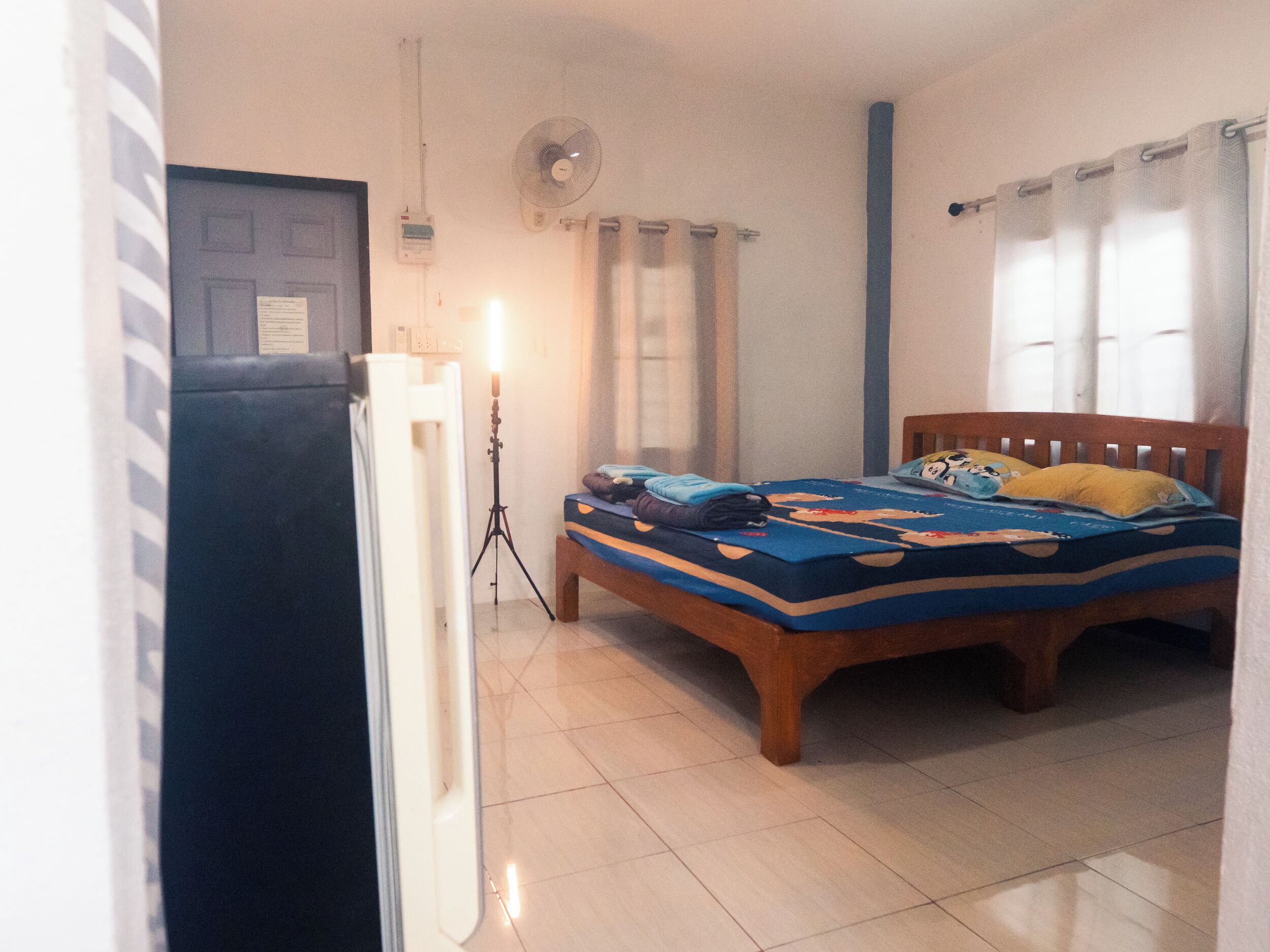 Un dormitorio con cama, ventilador, puerta y ventana con cortinas.