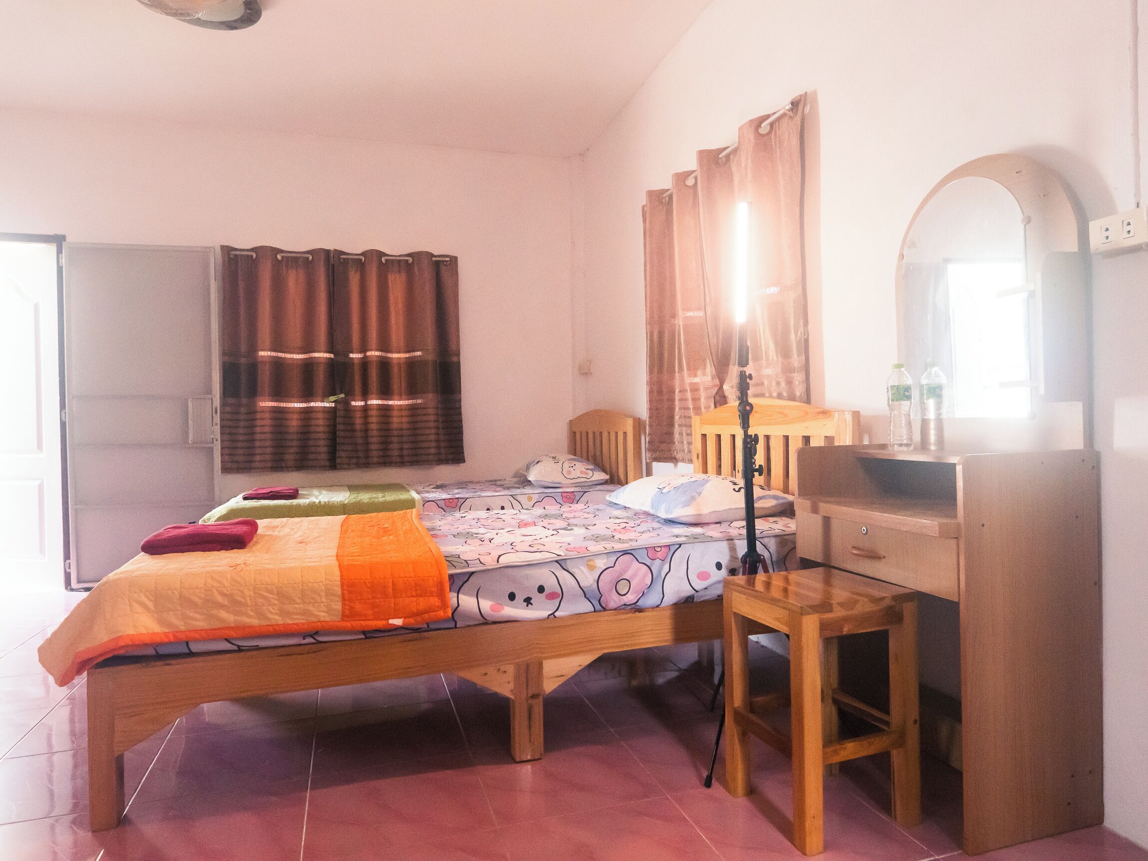 A bedroom with a wooden bed, a desk, a chair, a mirror, and a window with curtains.