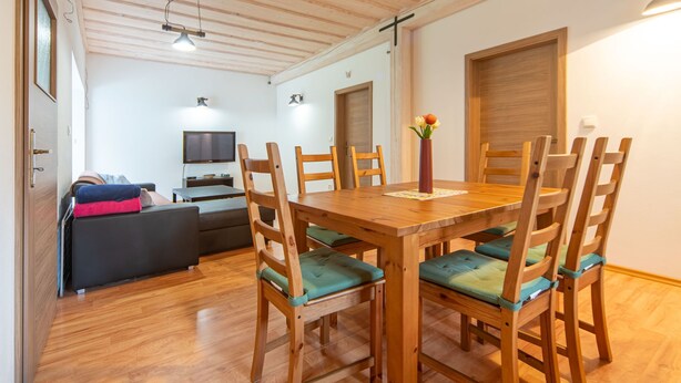 Un comedor con una mesa y sillas de madera, un televisor y un sofá al fondo.