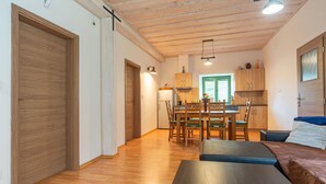 Amplia sala de estar con piso de madera, una mesa de comedor con sillas, un sofá y un área de cocina con gabinetes de madera y una ventana.