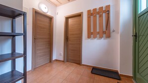 Un pasillo con puertas de madera, un perchero en la pared, un felpudo negro y un estante metálico.