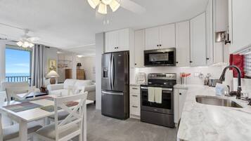 A modern kitchen with white cabinets, stainless steel appliances, and a large window overlooking the sea.