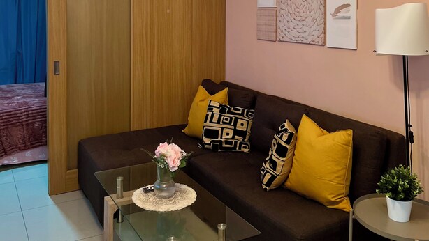 Een moderne woonkamer met een glazen salontafel, een bruine bank met kussens met een patroon, een houten deur en een plafondlamp.