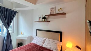 Een slaapkamer met een bed, nachtkastje, lamp en een raam met gordijnen.