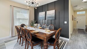 A dining area with a wooden table set for six, flanked by dark paneling and two framed artworks.