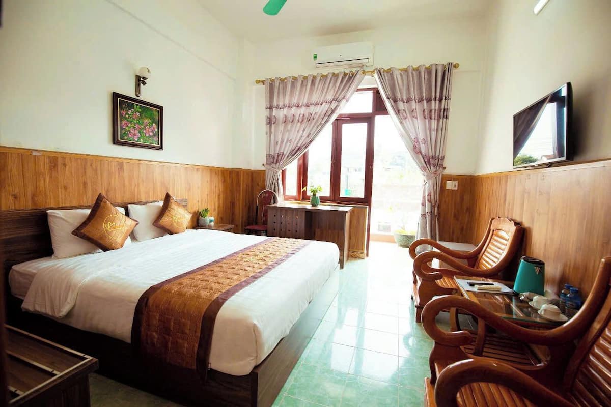 A hotel room with a wooden bed, a desk with a chair, a TV, and a window with curtains.