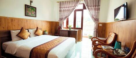 A hotel room with a wooden bed, a desk with a chair, a TV, and a window with curtains.