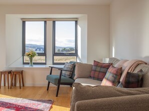 Ein Wohnzimmer mit Sofa, Sessel, kleinem Tisch und einem Fenster mit Landschaftsblick.
