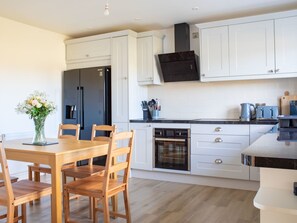 Una cocina moderna con armarios blancos, campana extractora negra, electrodomésticos de acero inoxidable y una mesa de comedor de madera con sillas.