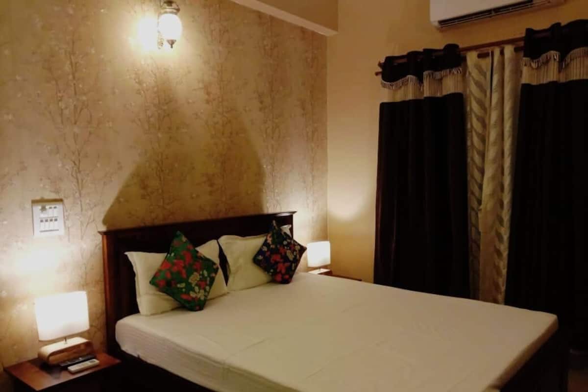 A hotel room with a large bed, two bedside lamps, a nightstand, and a wall-mounted air conditioner.