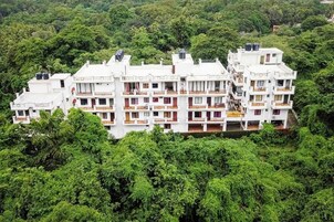 Un edificio residencial de varios pisos con balcones, rodeado de abundante vegetación.