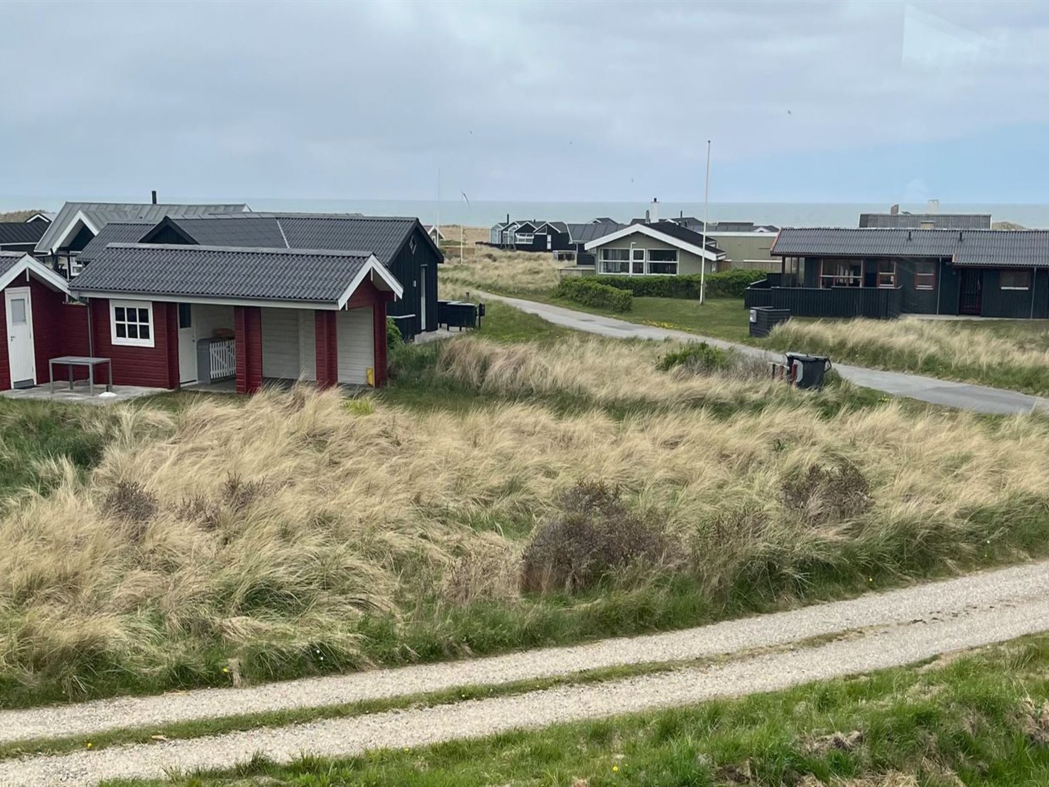Eine Küstenlandschaft mit mehreren kleinen Häusern, einem Kiesweg und Blick auf das Meer.