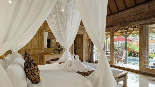A luxurious bedroom with a canopy bed, wooden paneling, and a view of an outdoor patio. - Astala Ubud Villa (Ubud)