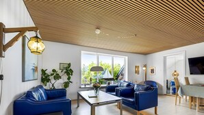 Una sala de estar moderna con techo de madera inclinado, sofás de cuero azul, una mesa de centro y una zona de comedor con televisor y mesa.
