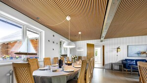 Un comedor moderno con techo de madera, un ventanal grande y un sofá azul al fondo.