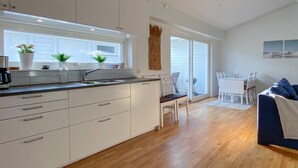 A modern kitchen with white cabinetry, a built-in stove, and a window with potted plants.