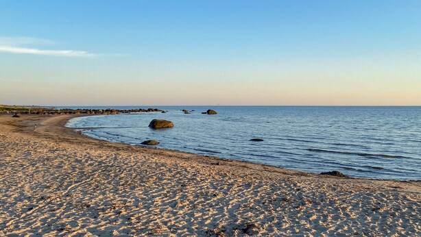 A sandy beach with large rocks in the water and a clear sky.