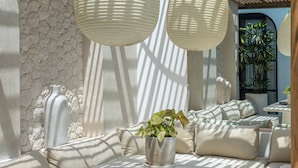 En utomhusplats med sittplatser, en pergola, en stenmur och hängande lampor.