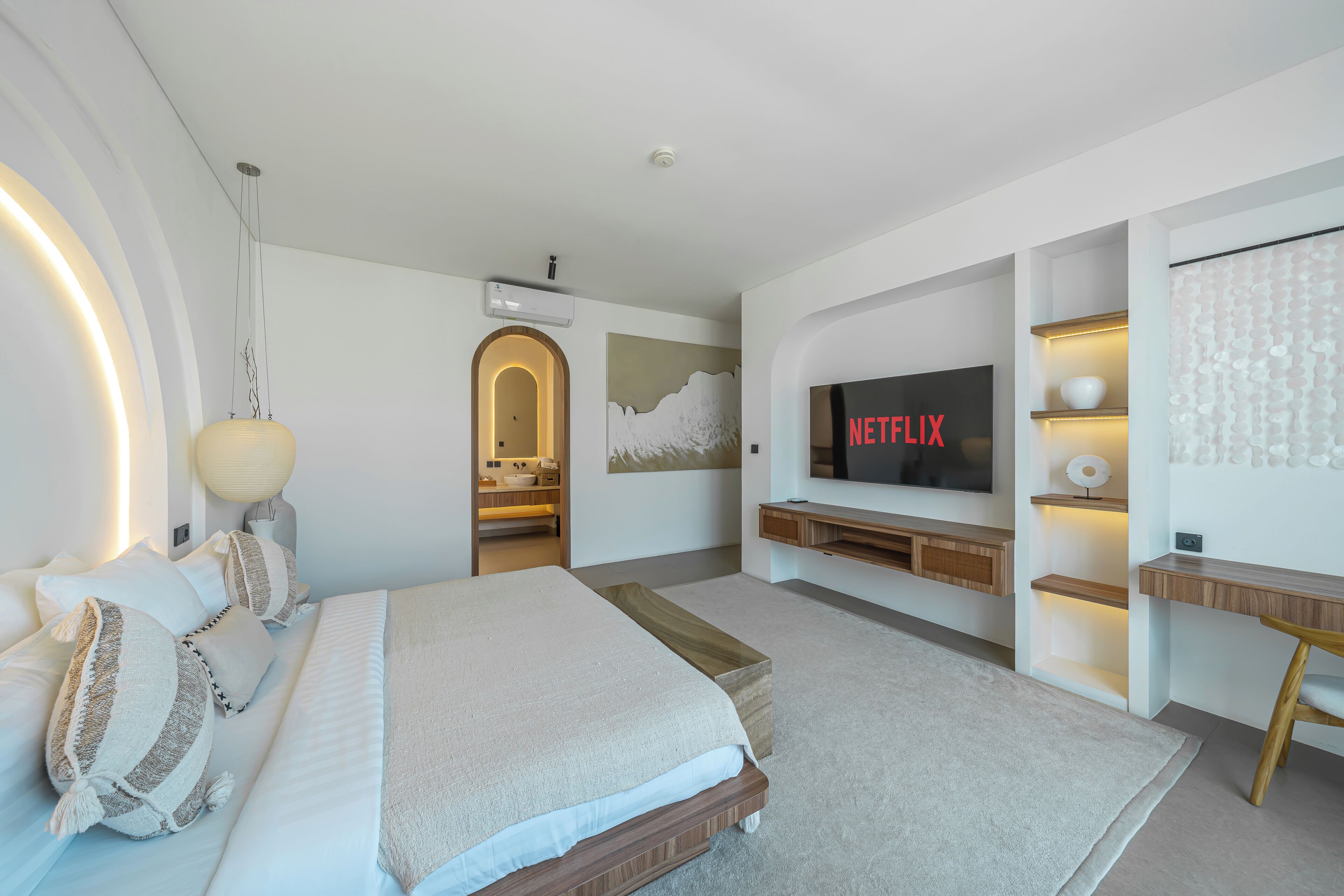 A modern hotel room with a large bed, a TV, a desk, and a wall-mounted shelf.