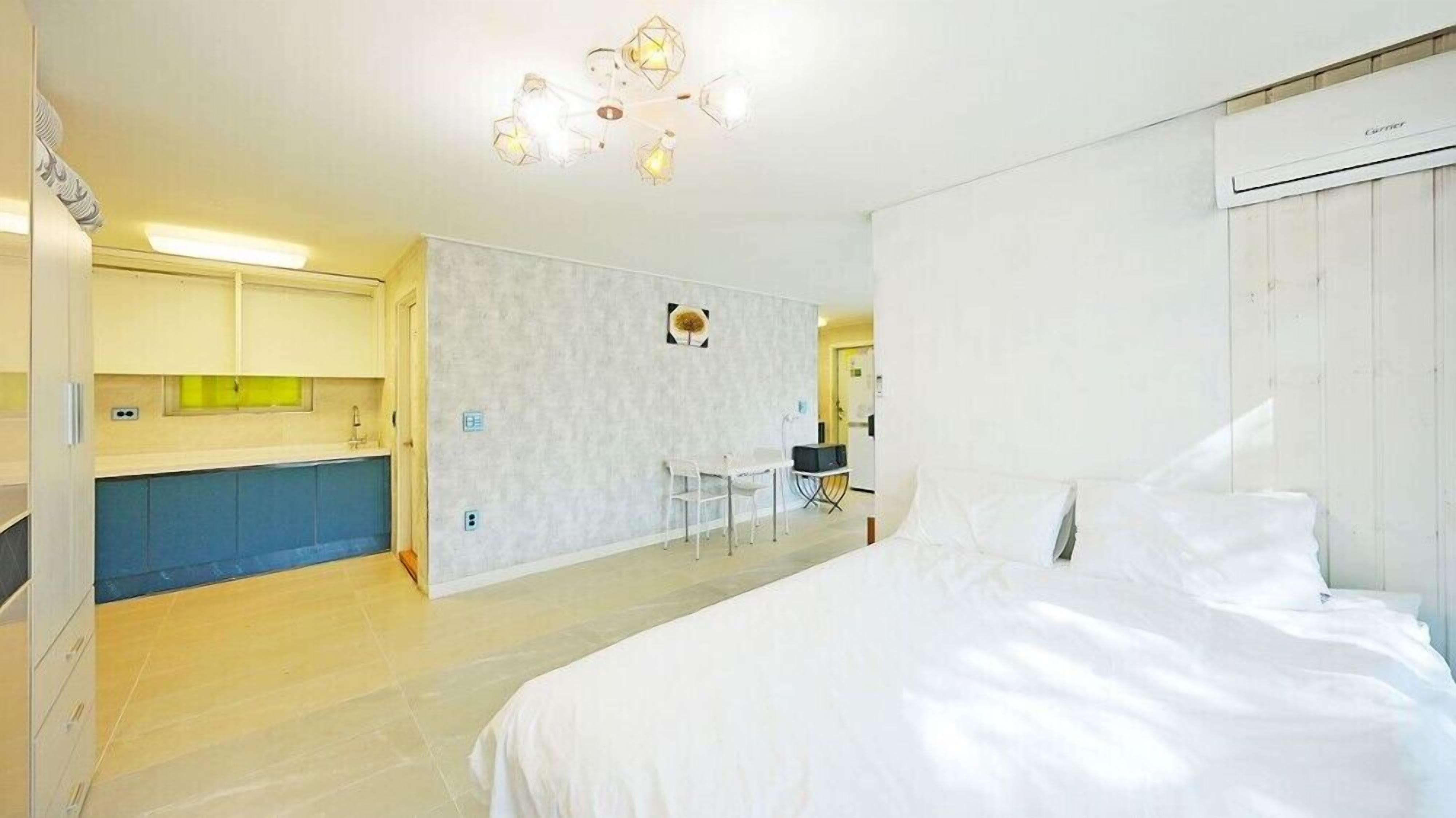 A modern hotel room with a large bed, a small desk, and a kitchenette.