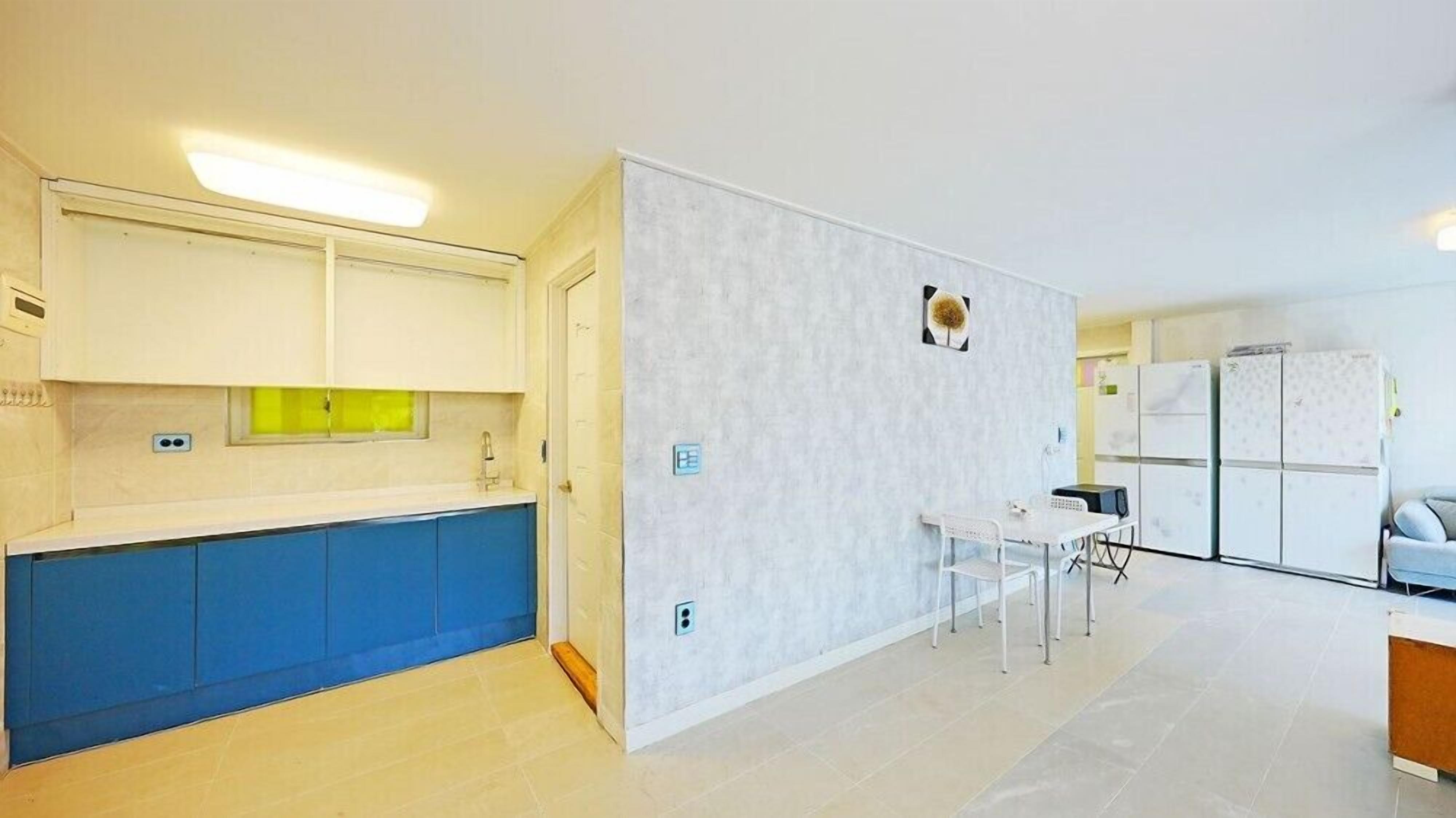 A modern kitchen with blue cabinets, a white countertop, and a small dining area with a table and chairs.