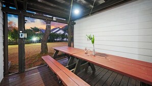Une terrasse extérieure en bois, avec une table de pique-nique, un pot de fleurs et une vue sur un coucher de soleil au-dessus d’un quartier résidentiel.