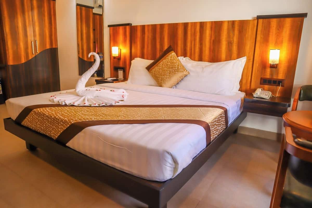 Habitación de hotel con una cama grande, cabecero de madera, dos mesitas de noche con lámparas y una decoración de cisne sobre la cama.