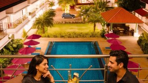 Una pareja sentada en una mesa con vista a la piscina, rodeada de sombrillas y un espacio exterior bien iluminado.