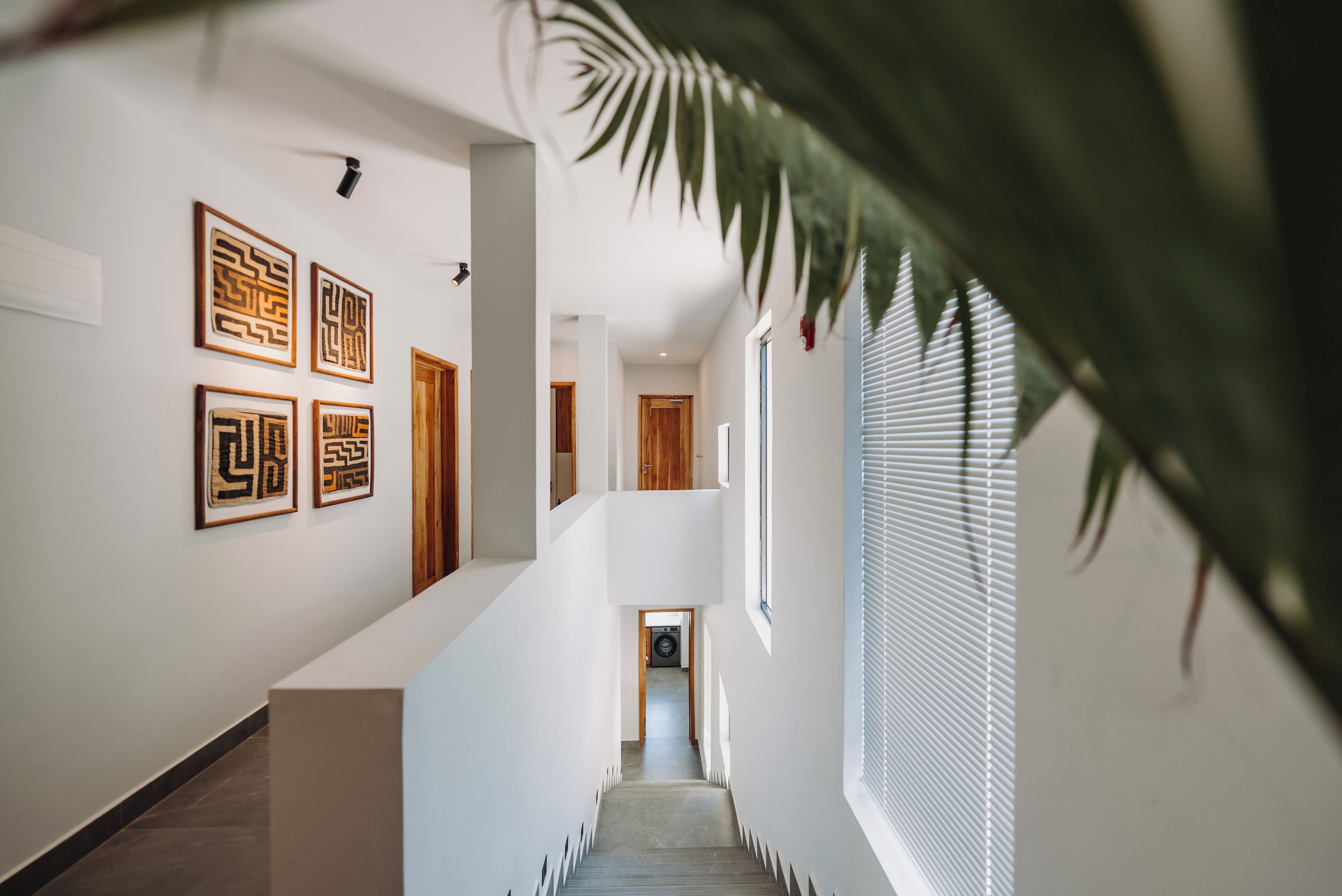 A modern interior with a staircase, framed artwork on the walls, and a view into another room.