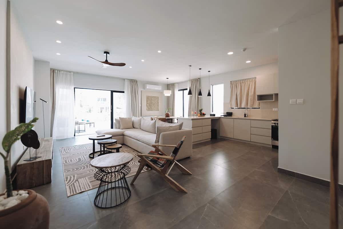 Moderni olohuone, jossa on sohva, sohvapöytä ja tuoleja, keittiöalue kaappeineen ja kodinkoneineen sekä ruokailutila pöydän ja tuolien kera.