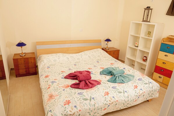 A neatly made bed with floral bedding, two bedside tables with lamps, a wooden dresser, and a white shelving unit.