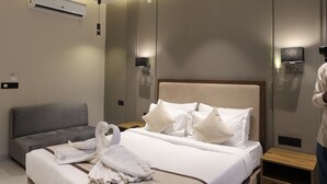 Egy modern szállodai szoba, amelyben egy nagy ágy, egy éjjeliszemélyzet, egy lámpás, egy mennyezeti ventilátor, egy légkondicionáló és egy a falra szerelt lámpatest található.