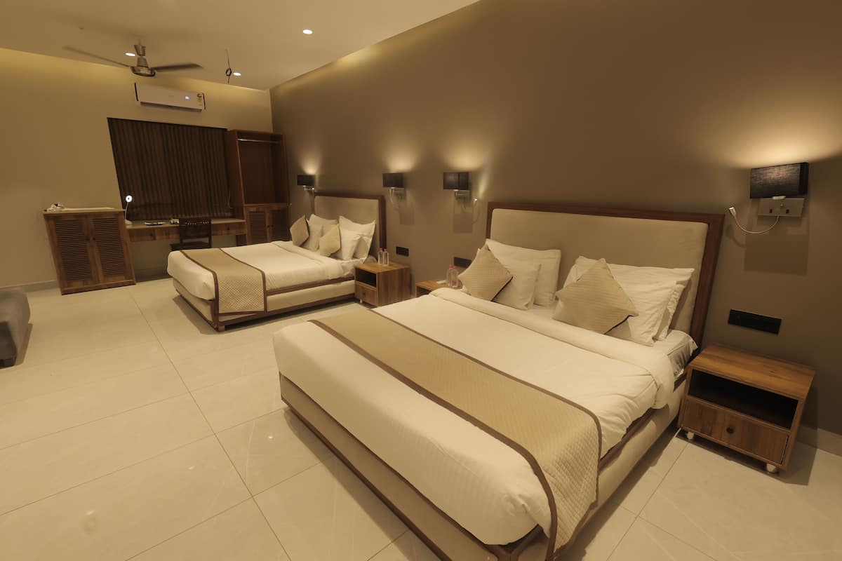 A hotel room with two beds, a desk, a wardrobe, and a ceiling fan.