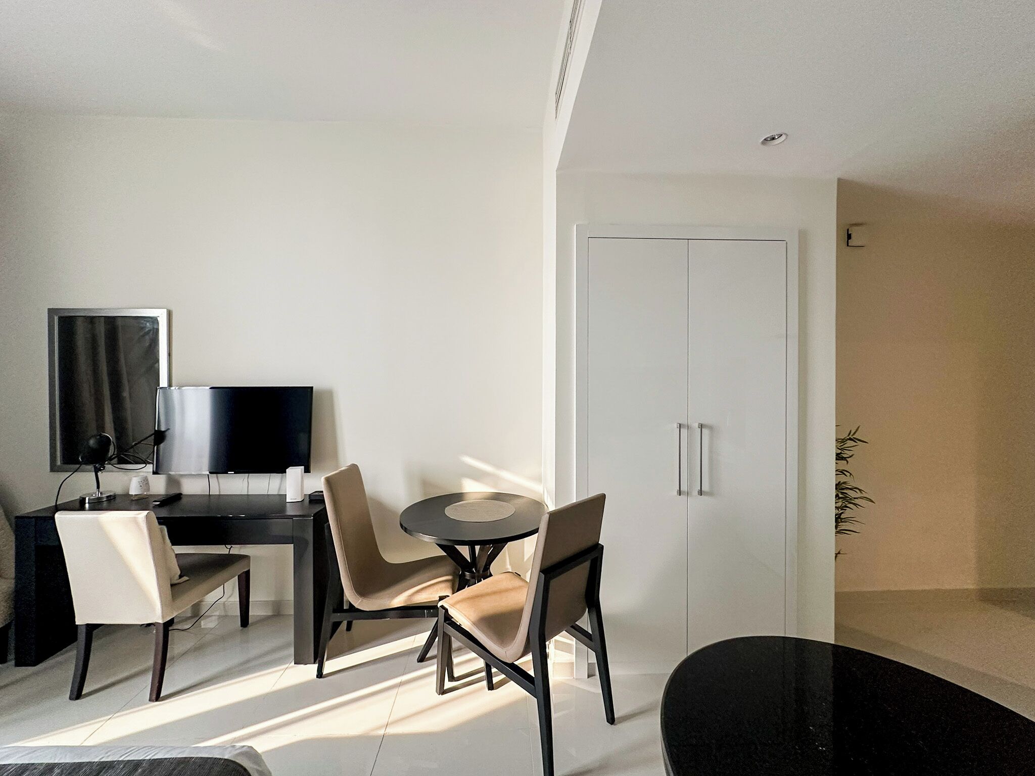 Een moderne, goed verlichte kamer met een eettafel, stoelen, een televisie en een kledingkast.