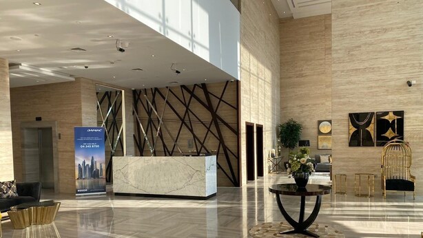 A spacious lobby with a reception desk, modern furniture, and a large window allowing natural light. - Bespoke Residences - Tower 108 JVC (Dubai)