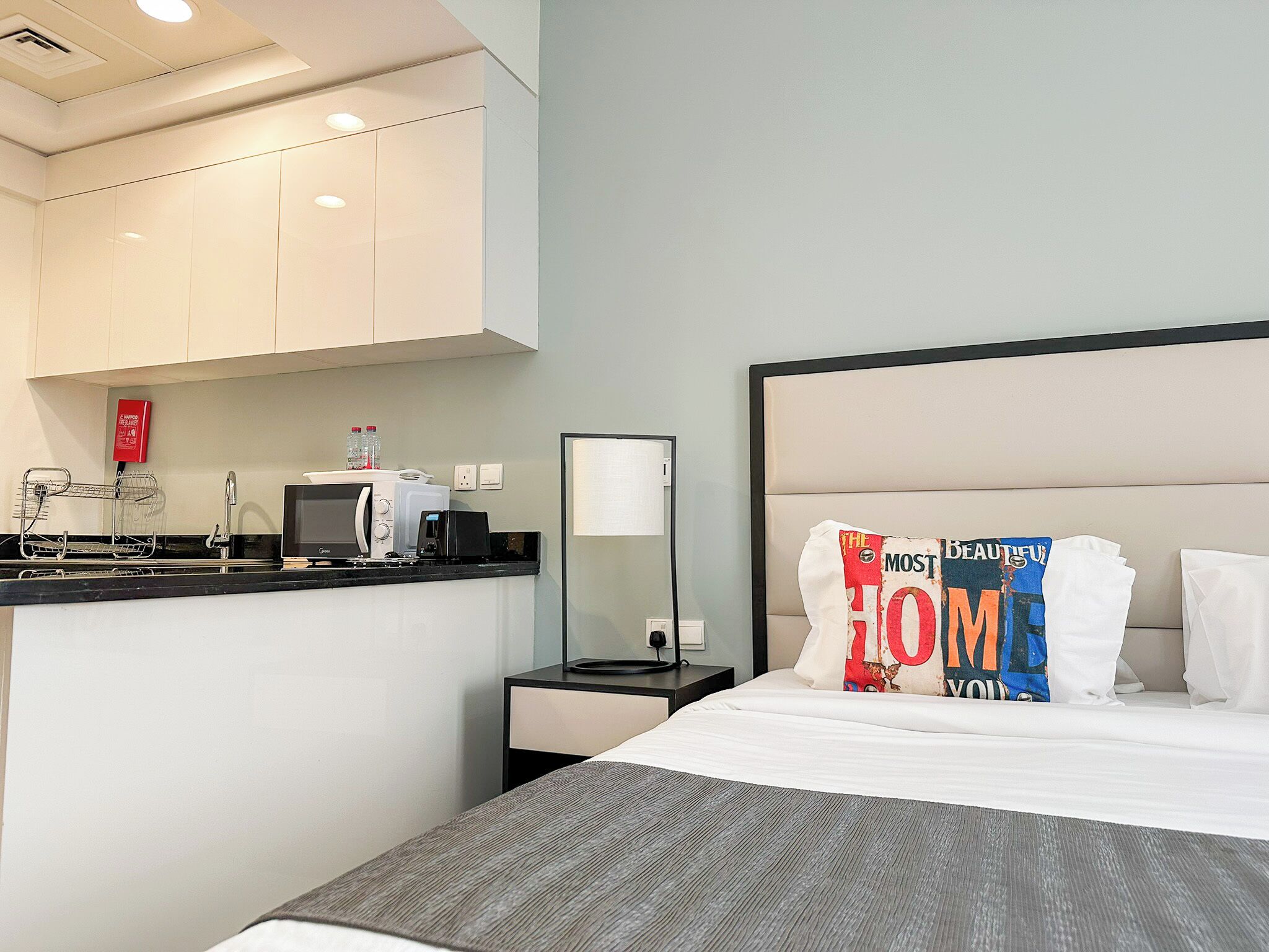 Een hotelkamer met een bed, nachtkastje, bureau met computer, magnetron en een klein kitchenette.