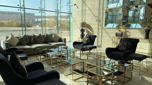 A modern lounge with a sofa, armchairs, and a coffee table, featuring glass partitions and a view of the outside. - Bespoke Residences - Tower 108 JVC (Dubai)