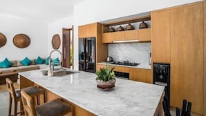 A modern kitchen with wooden cabinets, a marble countertop, and a built-in stove. - Villa Mugiwara by BaliSuperHost (Ubud)