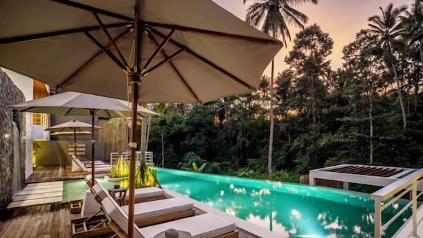 A poolside area with lounge chairs, umbrellas, and a view of a natural landscape. - Villa Mugiwara by BaliSuperHost (Ubud)