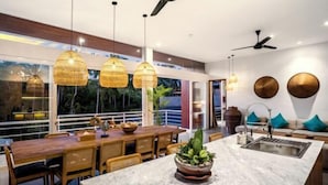 A modern kitchen with a marble island, wooden dining table, and wicker pendant lights. - Villa Mugiwara by BaliSuperHost (Ubud)