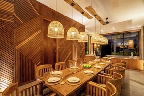 Un espace de salle à manger moderne, avec une longue table en bois, des suspensions en rotin et un lambris en bois.