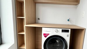 A compact laundry room with a built-in washing machine, wooden shelving, and a small window. - Mice House (Cam Ly - Da Lat)