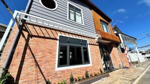 A two-story building with a brick facade, a large window with a white frame, and a small circular window above it. - Mice House (Cam Ly - Da Lat)