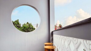 A balcony with a circular window, three wooden stools, and a patterned wall. - Mice House (Cam Ly - Da Lat)