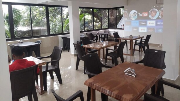 A spacious room with large windows, a wooden table, and several chairs. - JAS HOLIDAYS MORJIM (Morjim)