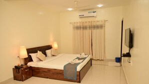 A neatly arranged bedroom with a bed, bedside tables, a TV, and a ceiling fan. - JAS HOLIDAYS MORJIM (Morjim)